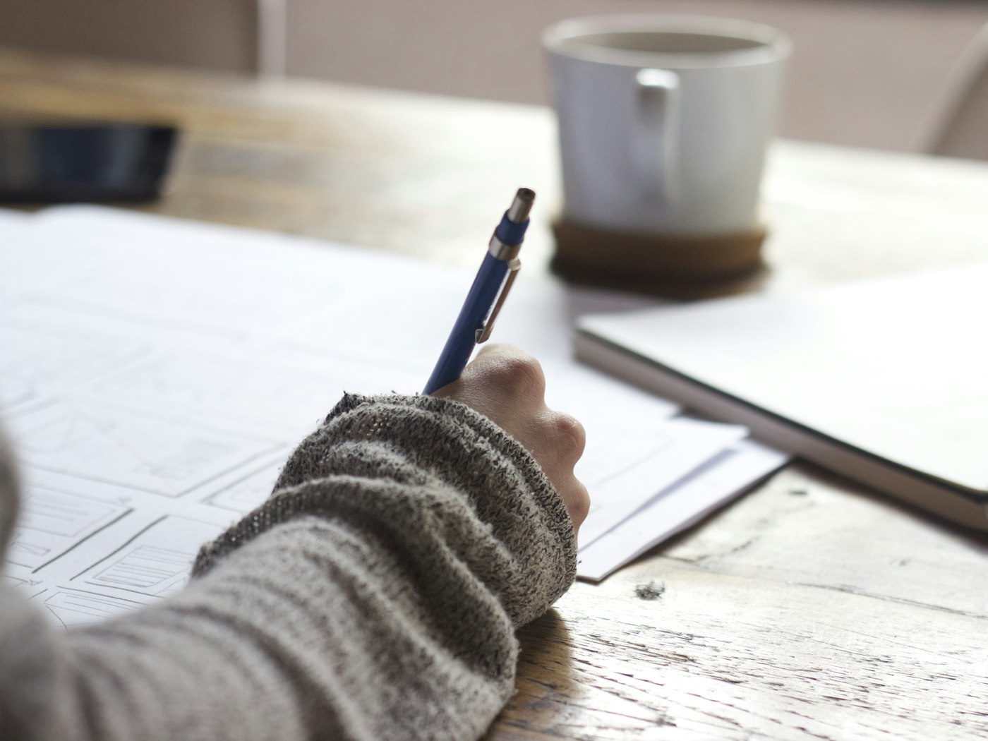 A person making notes beside a laptop and a cup of coffee